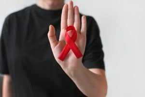 Pessoa exibindo um laço vermelho na palma da mão em apoio a campanha Dezembro Vermelho