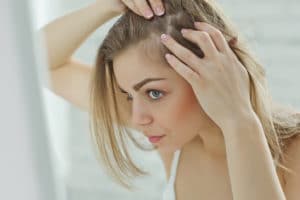 Mulher olhando no espelho enquanto mexe em seu próprio couro cabeludo preocupada com possível queda de cabelo